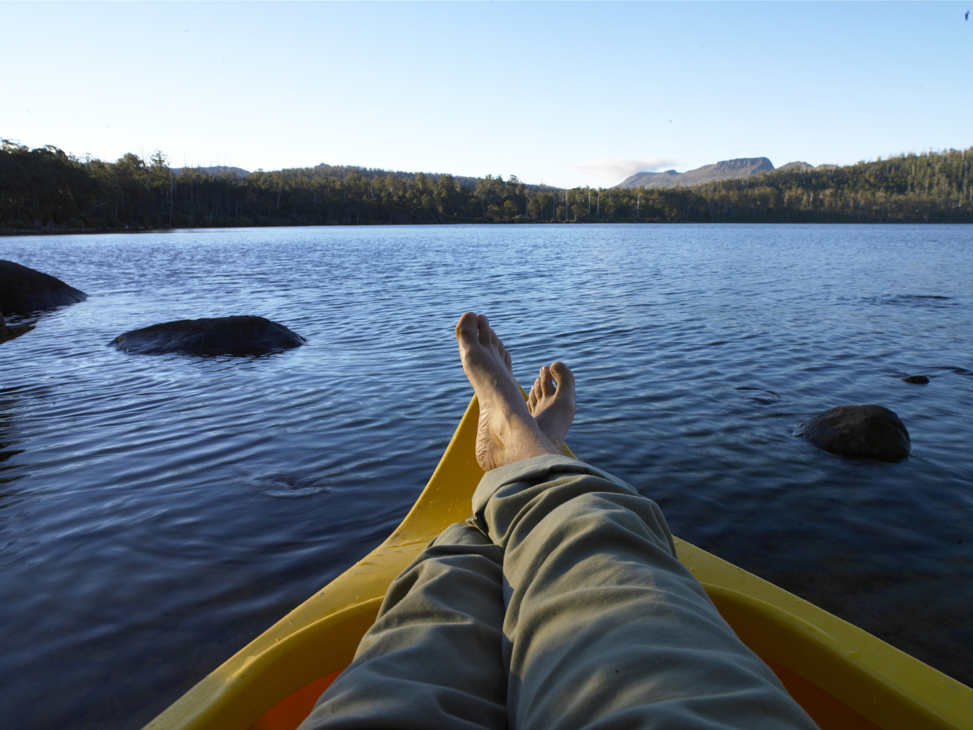 Taken from the view of the traveller, a man relaxes crossing his legs on a yellow kayak on Lake St Clair. 