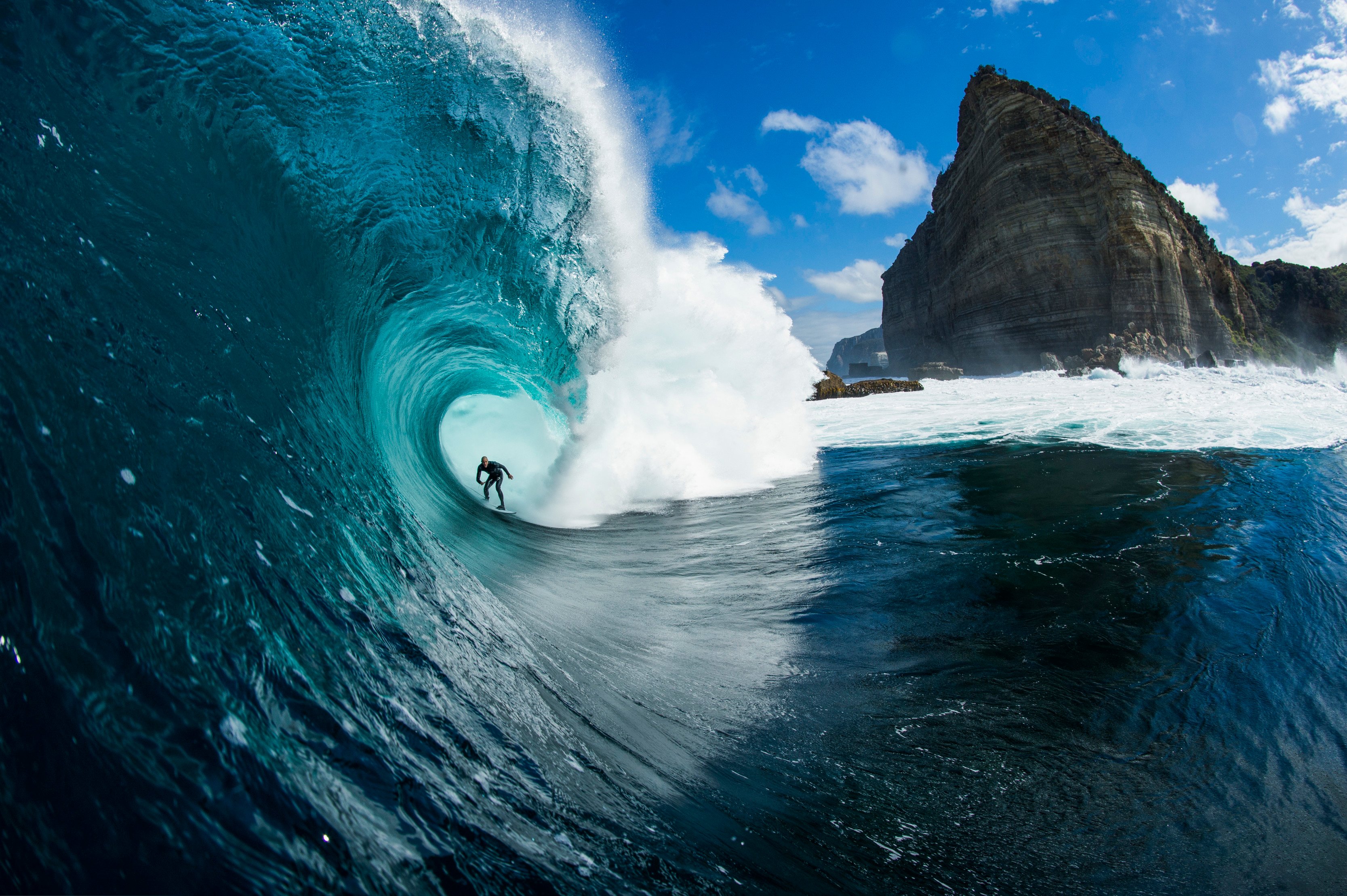 Looking down at a surfer getting barrelled by a large wave, with a prominent headland in the background, at Shipsterns Bluff, Tasman National Park.