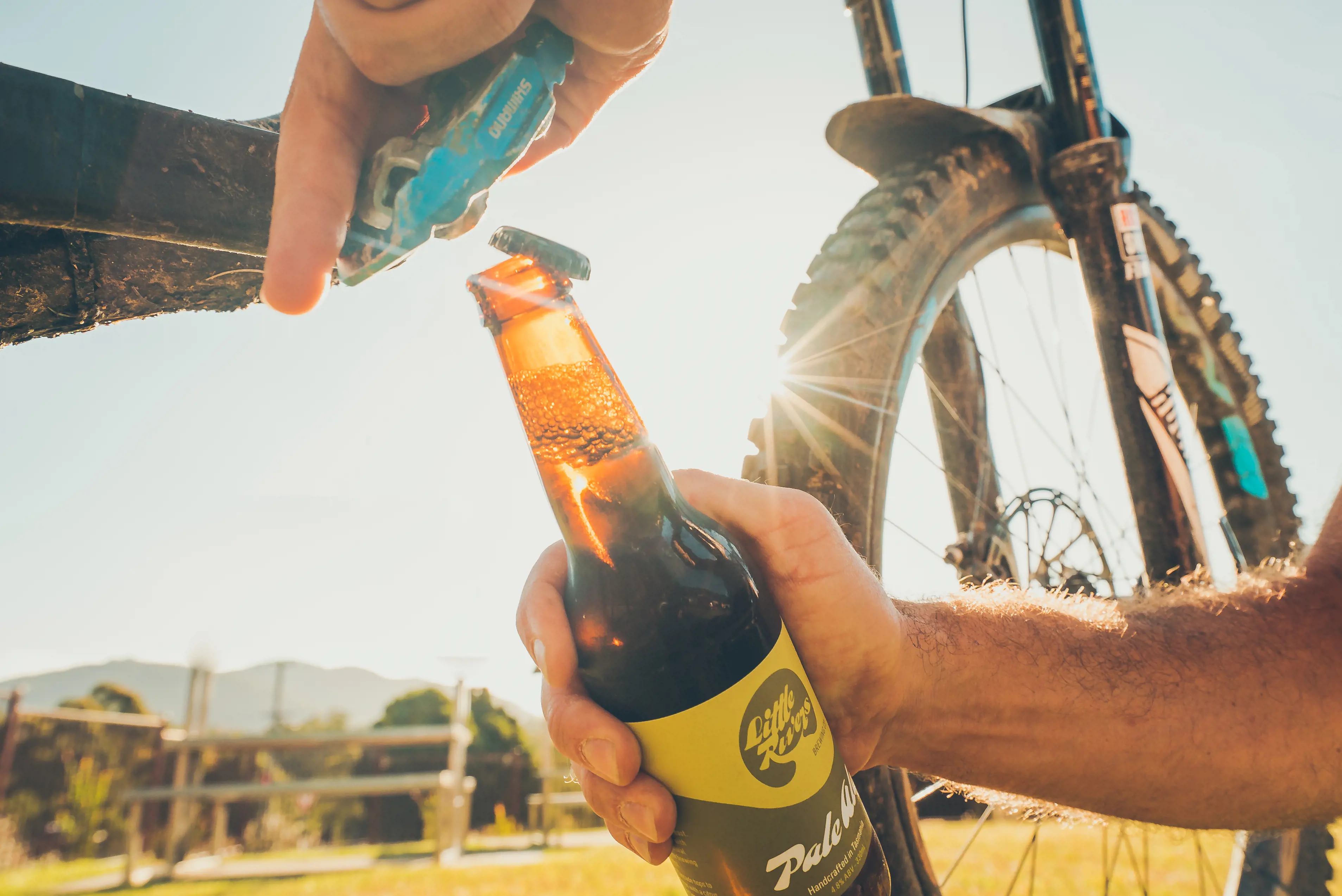 Person opening a Little Rivers beer with the pedal of a mountain bike.