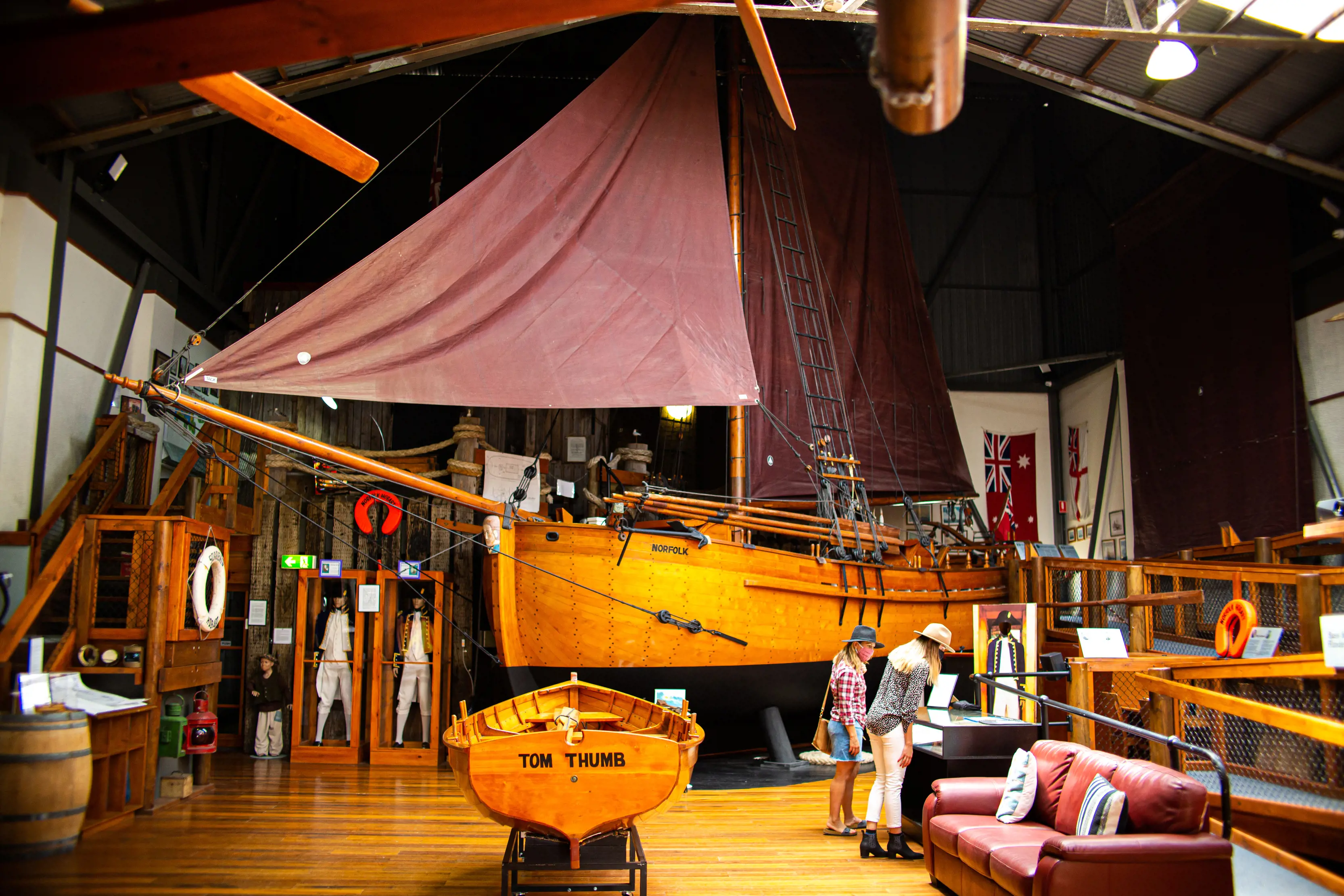 Inside a high-roofed museum room with several staircases and ramps to different levels. There are two wooden boats, uniforms and other maritime items on display.