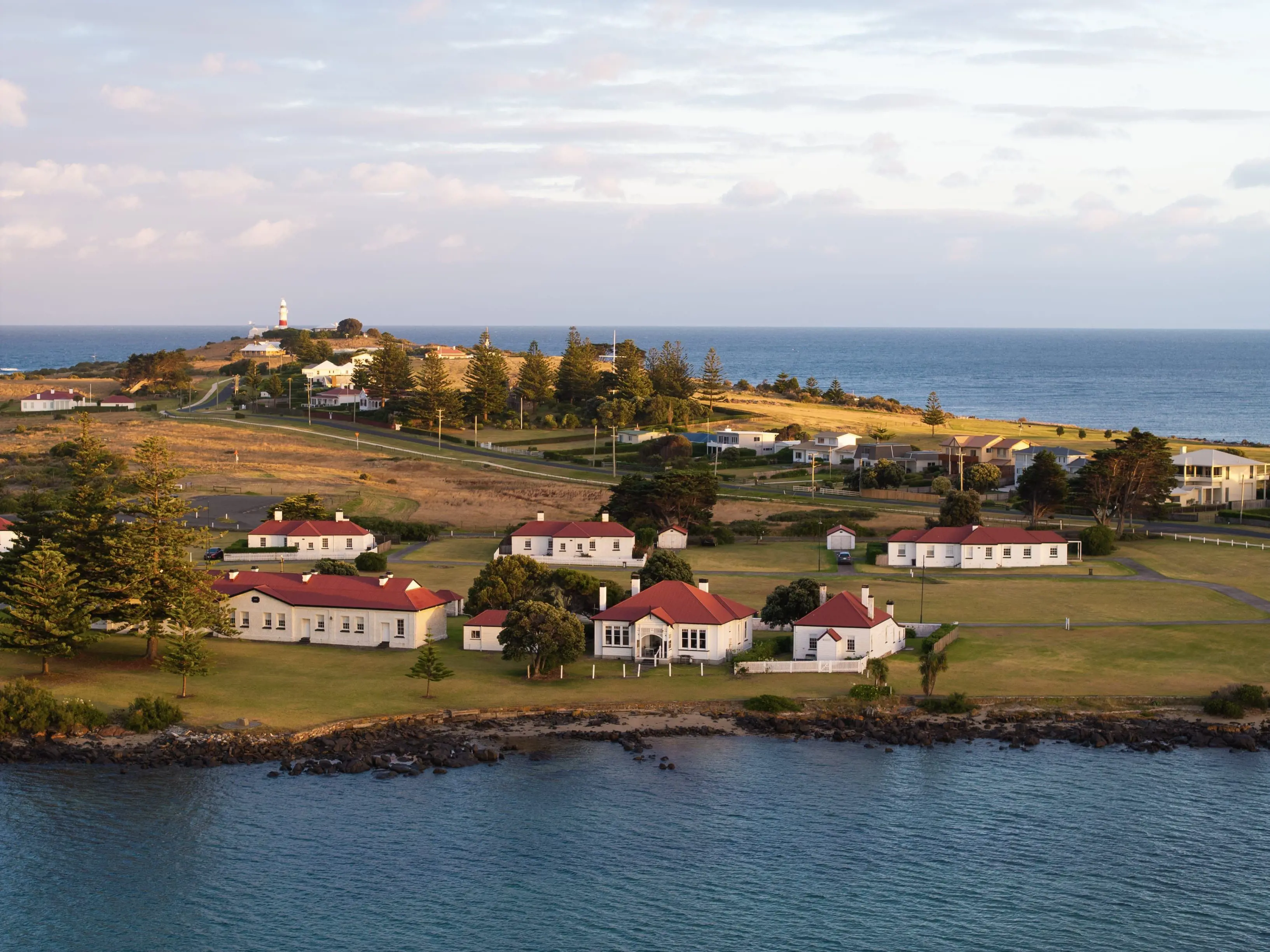 A piece of hilly land, dotted with trees, grass and buildings with white walls and red roofs. Water flows on either side.