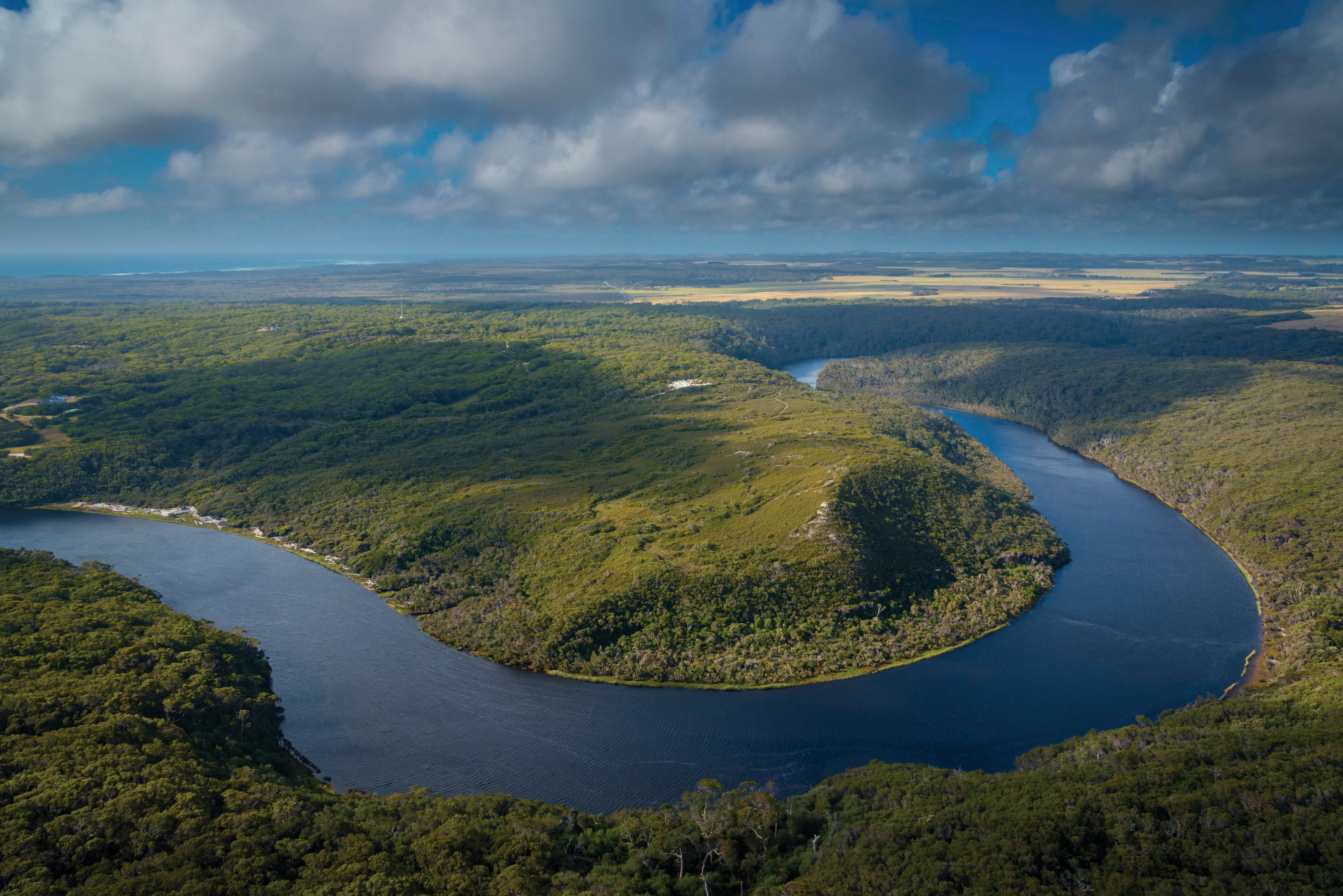 Birdseye view of Arthur River and surrounding trees, partially shadowed by clouds. 