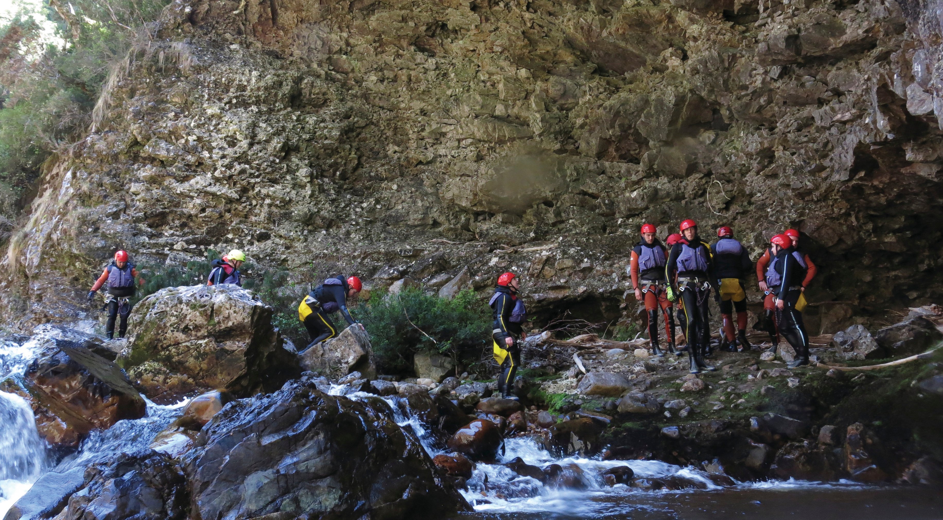 A group of tourists wearing safety gear, walk amongst the river and rocks in the Cradle Mountain Canyons.