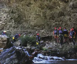 A group of tourists wearing safety gear, walk amongst the river and rocks in the Cradle Mountain Canyons.