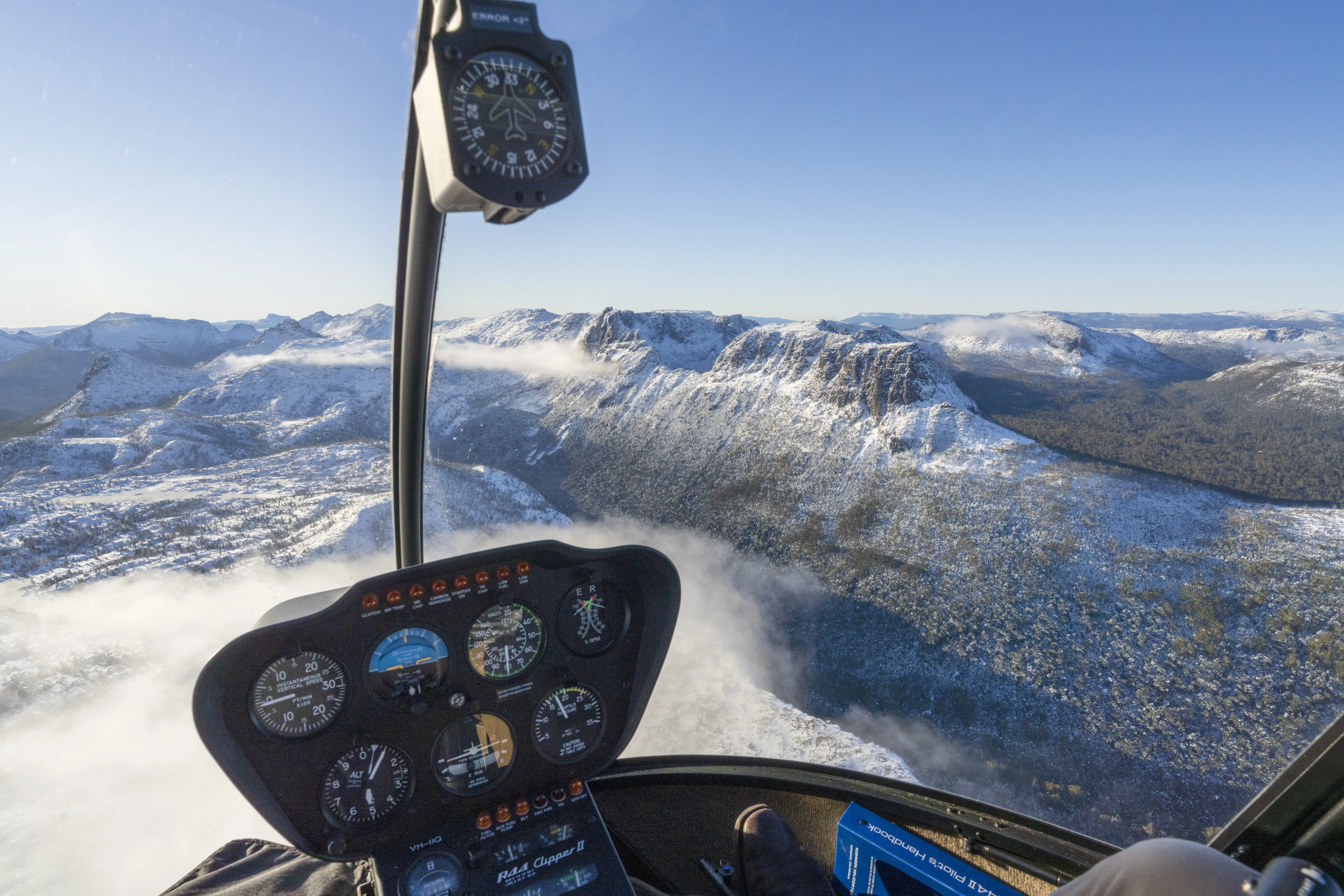 Breathtaking point of view image taken from a helicopter by Tasmanian Air tours of the mountains and surrounding nature, which is covered in snow.