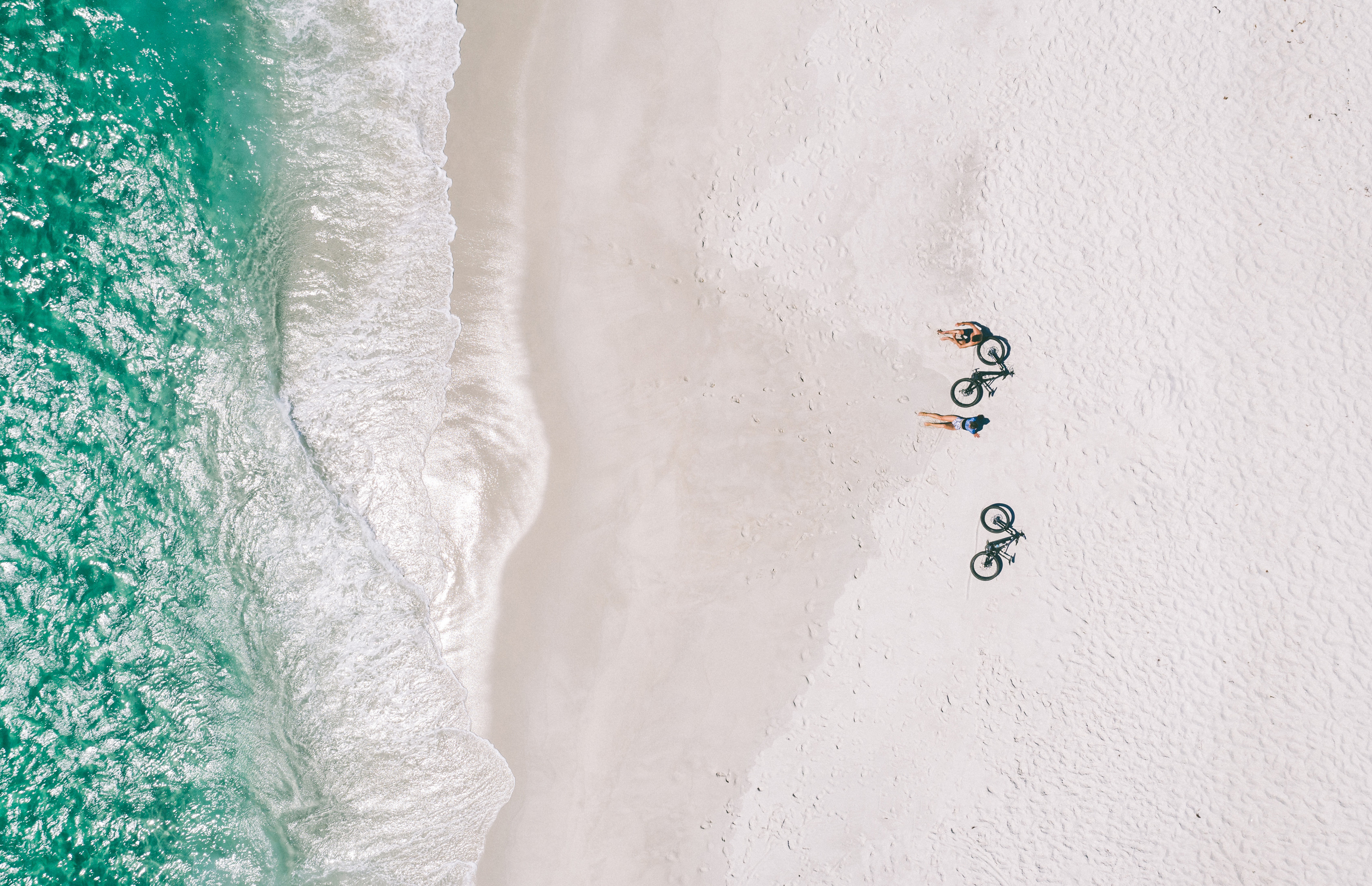 Ariel looking down over a beach at St Helens, two cyclists rest on sand with their bikes placed next to them facing the water.