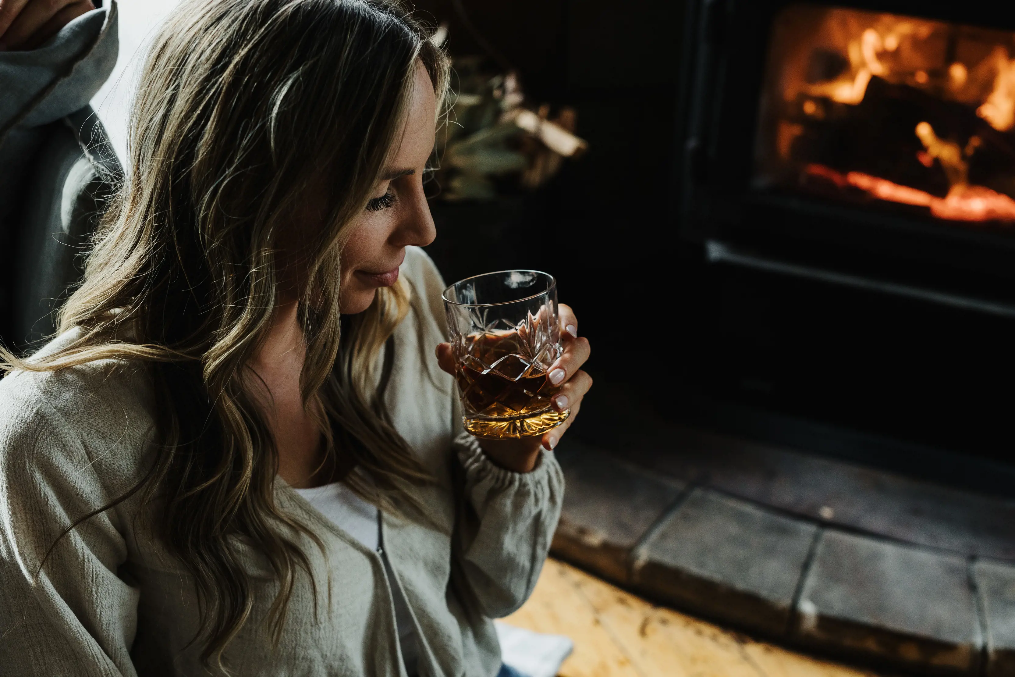 Close up of a female holding a glass of whisky indoors by the fire on Satellite Island, a small, privately-owned island.