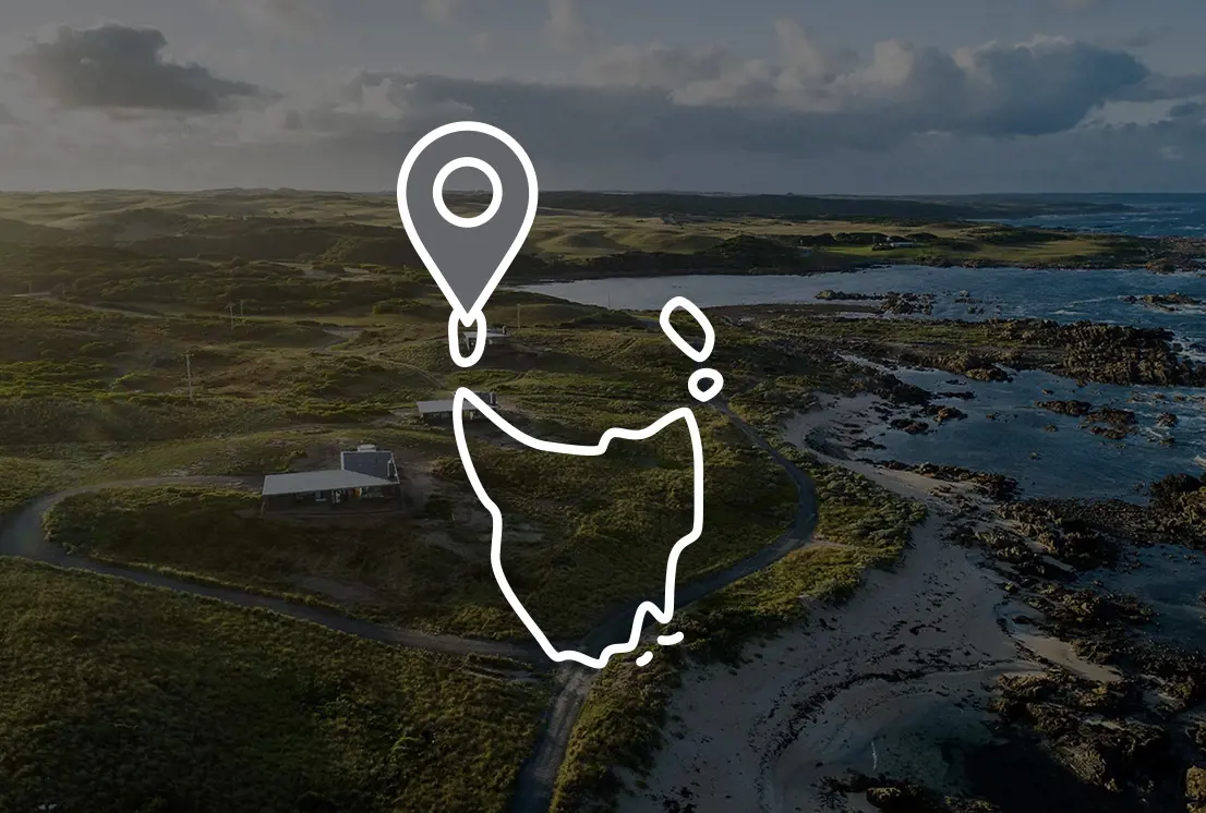 An aerial view of the jagged coastline and rocky shore. Overlaid is an icon of the outline of Tasmania with a map pin.