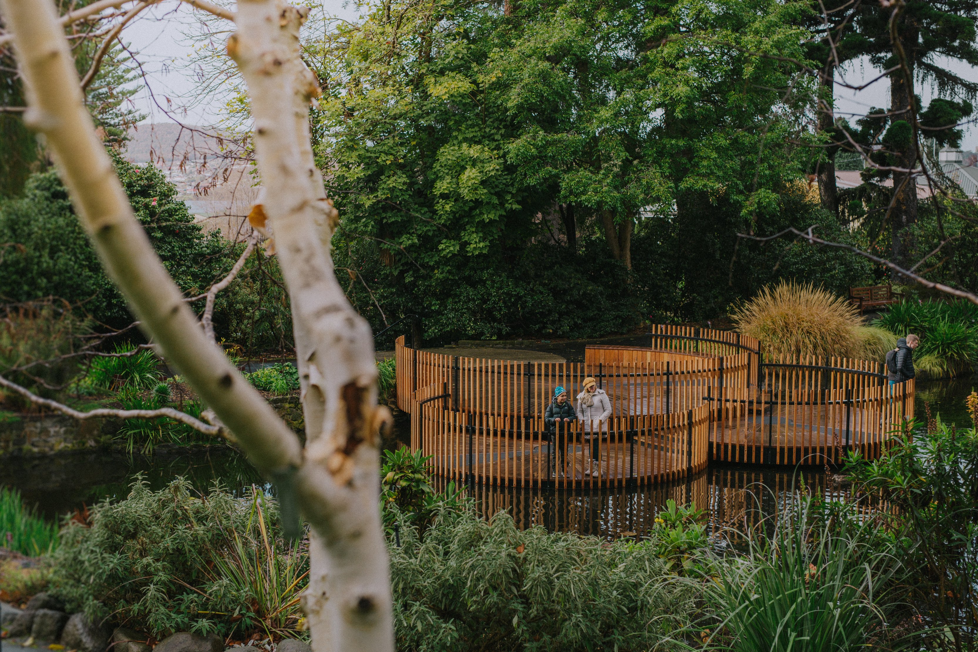 People stand on a wooden structure sitting atop a pond inside the Royal Tasmanian Botanical Gardens, Hobart. 