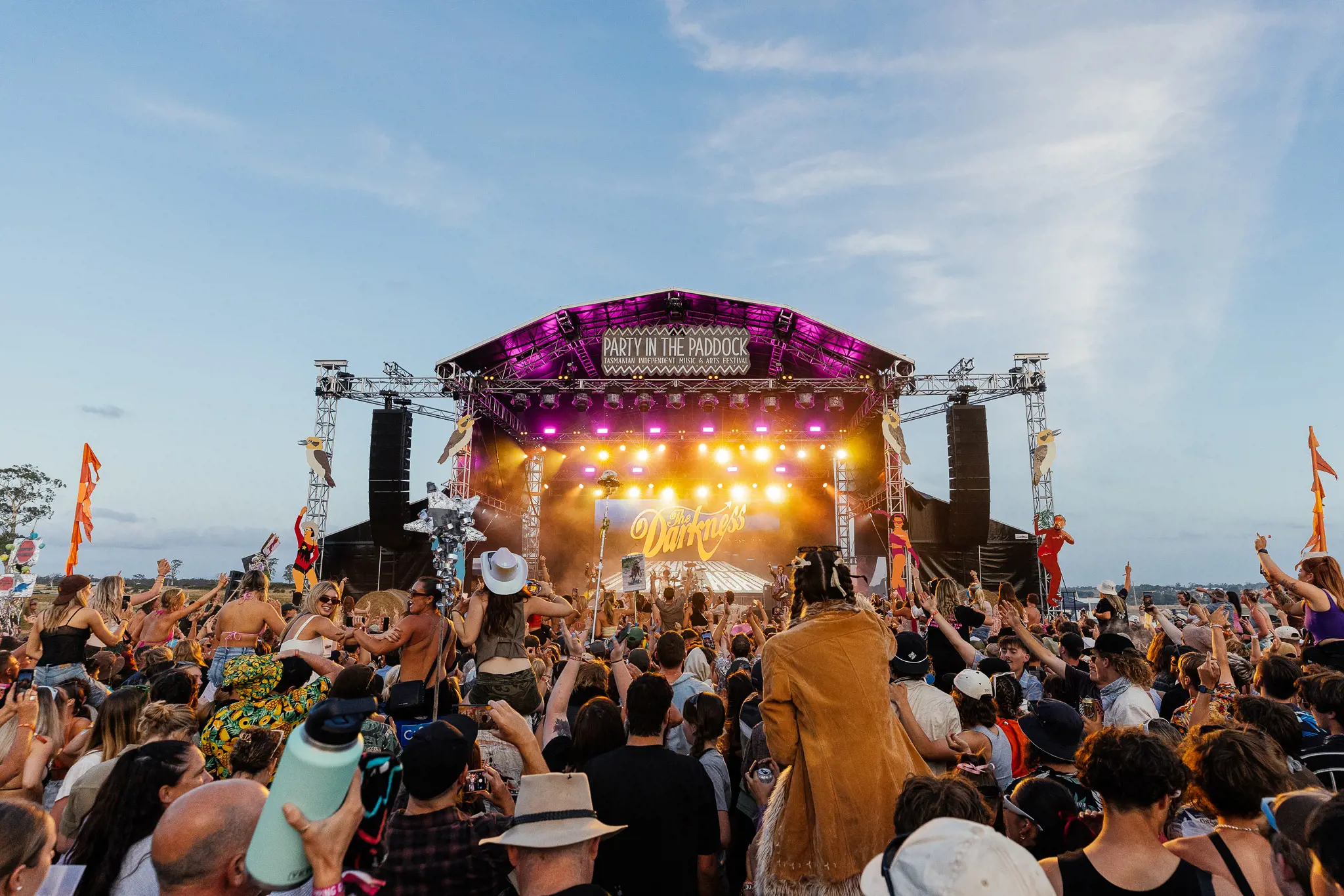 Behind a crowd of people, dancing and partying, looking up into the main stage of the Party in the Paddock music festival.