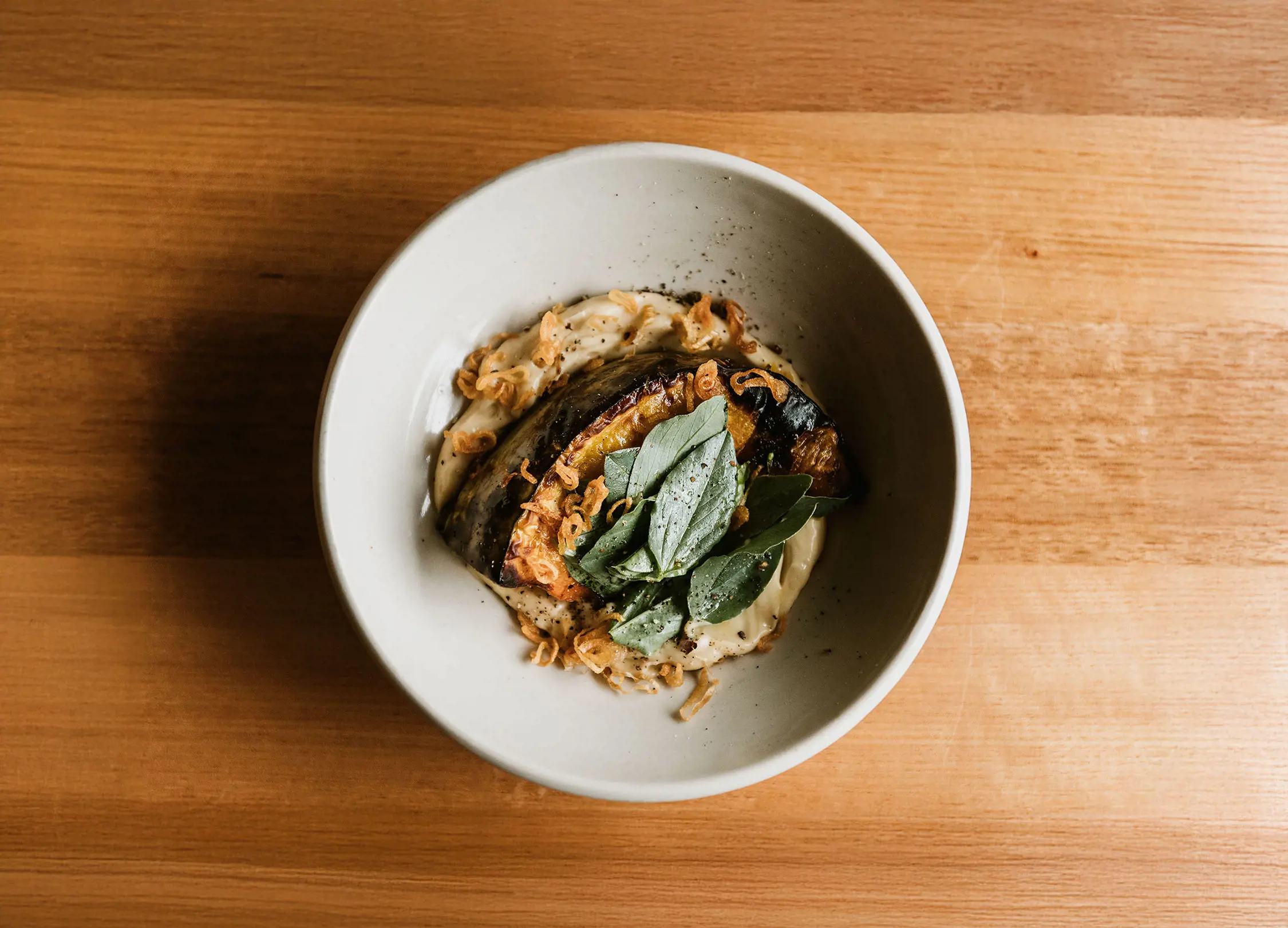 A top-down view of a delicious dish with herbs sprinkled on top, sitting on a smooth, light wood table.