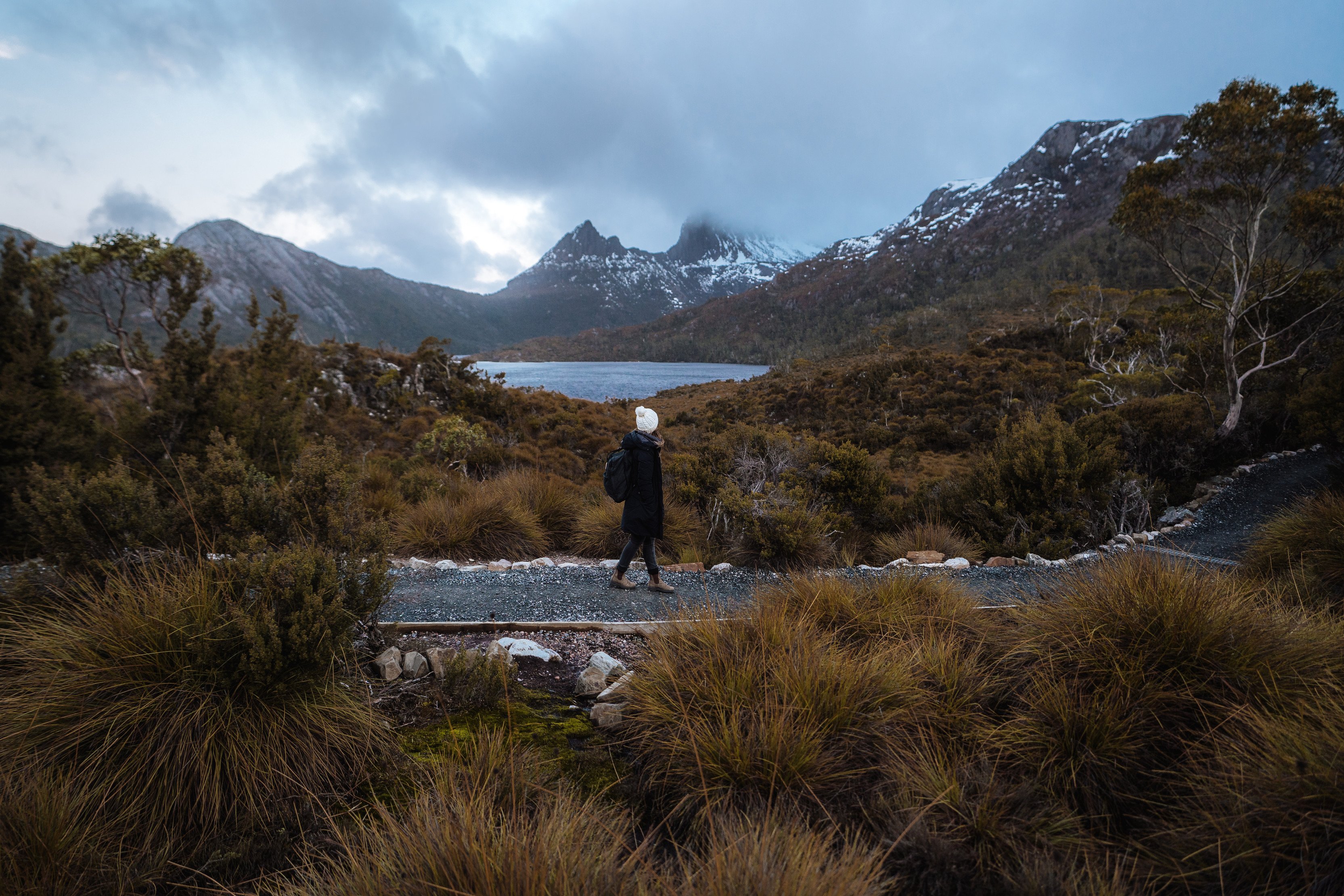 Person walking along a boardwalk track, surrounded by breathtaking landscape of mountains and forest, located in Cradle Mountain.