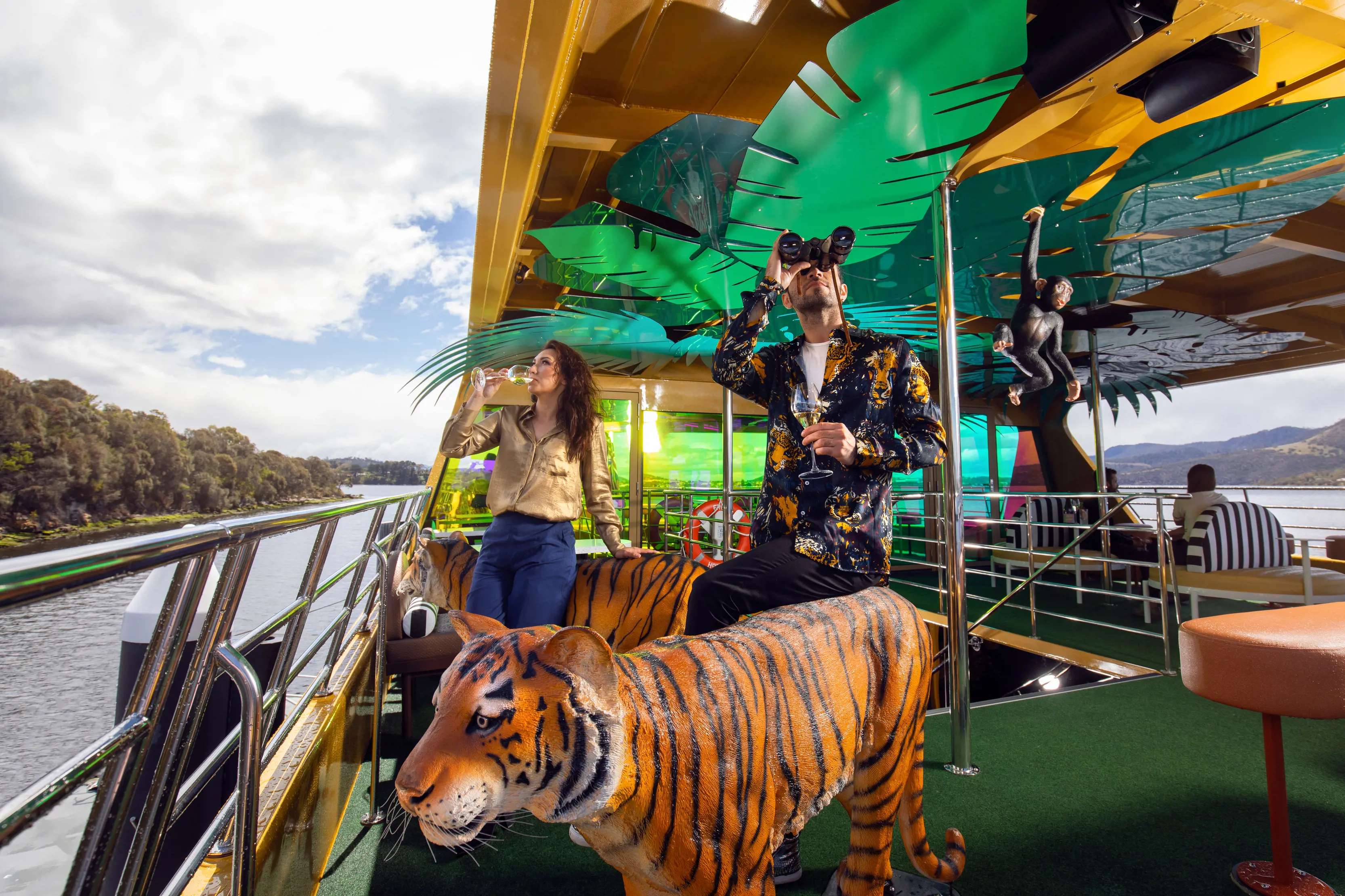 A man and woman sipping drinks on the top deck of Mona Roma ferry MR-II, the ferry has an exotic jungle, featuring tiger and monkey statues.