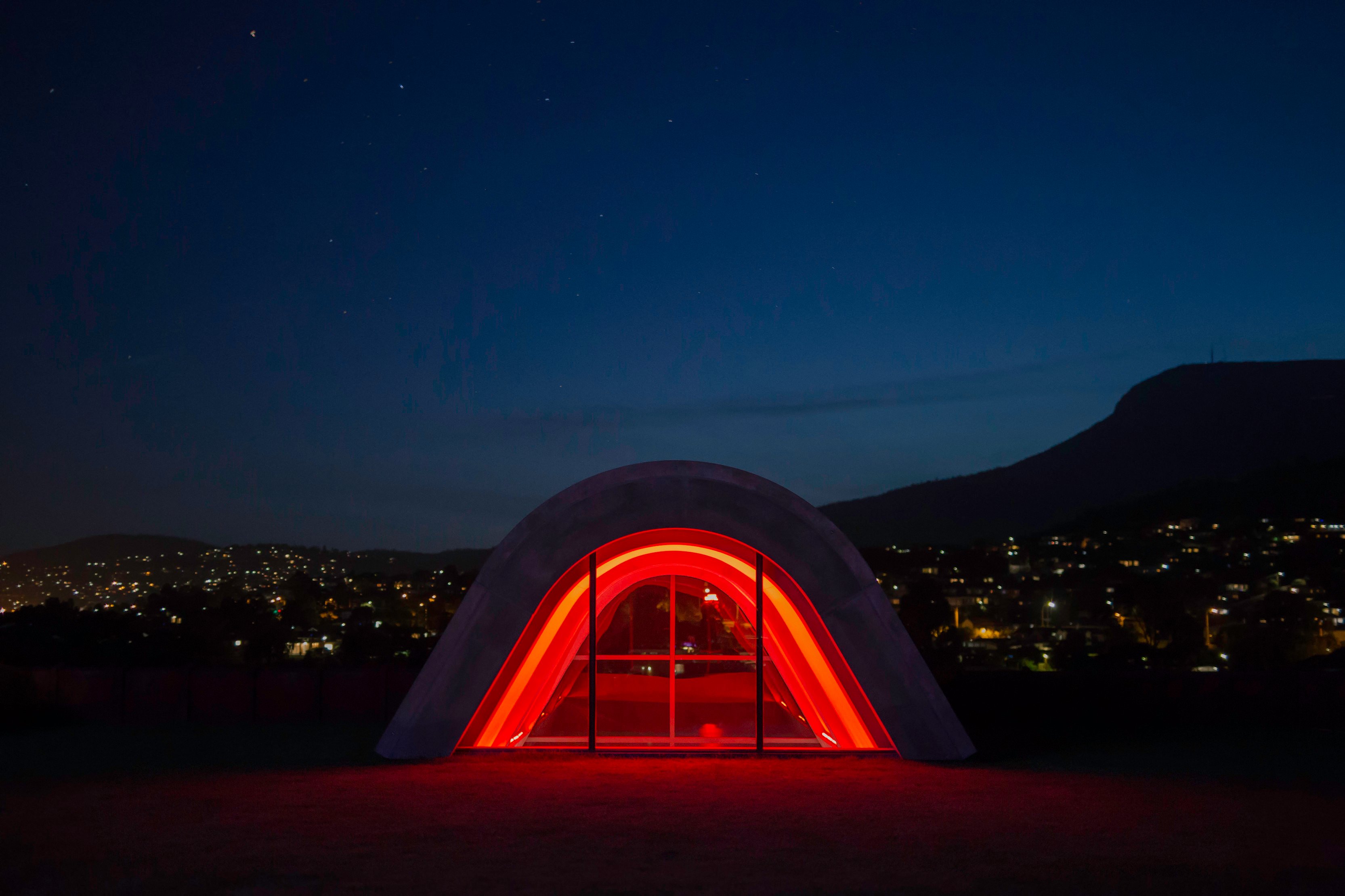 External night shot of the Pharos wing at Mona museum, lit up in red lights.