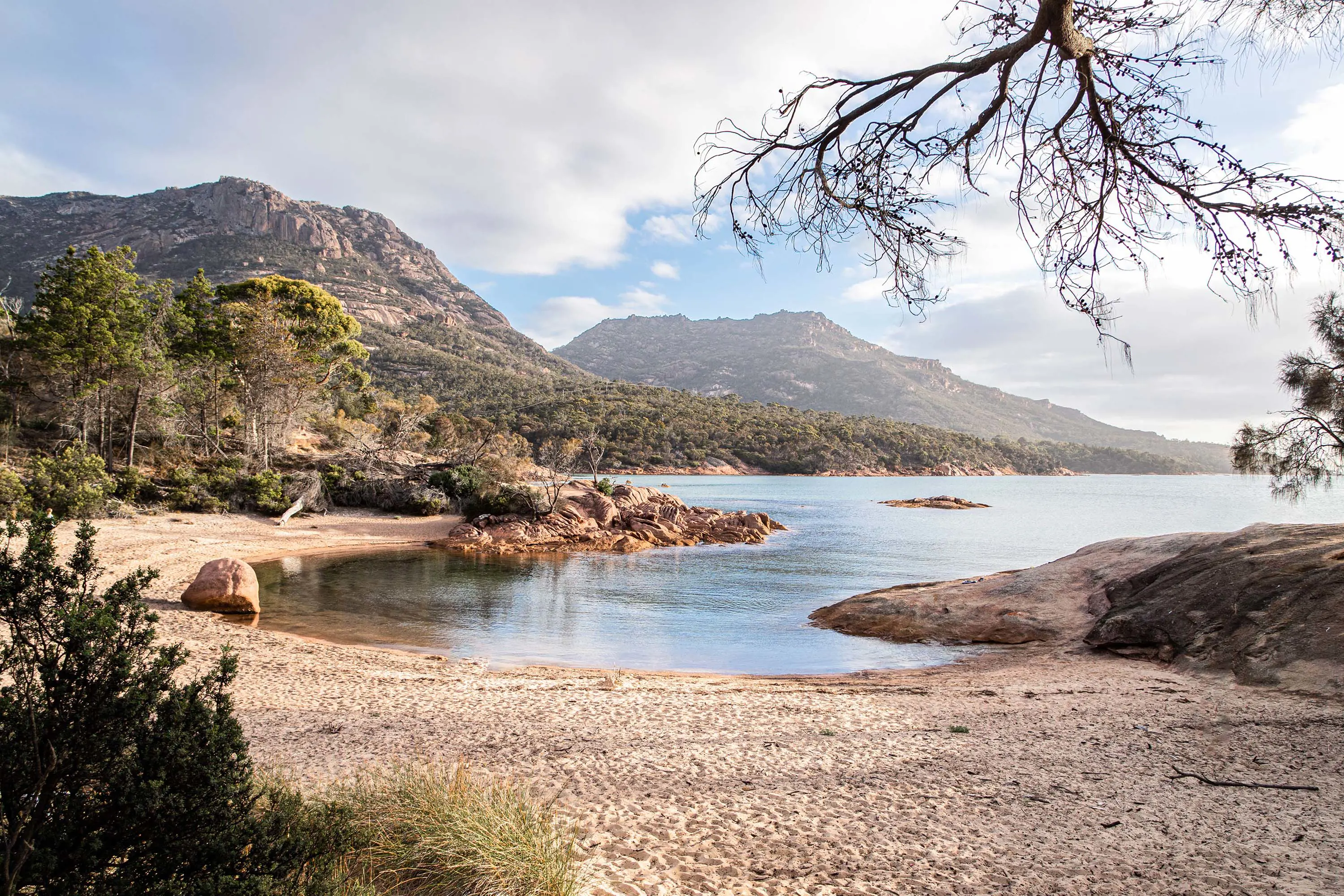 A serene beach panorama highlighting peaceful waters and impressive mountains on the horizon.