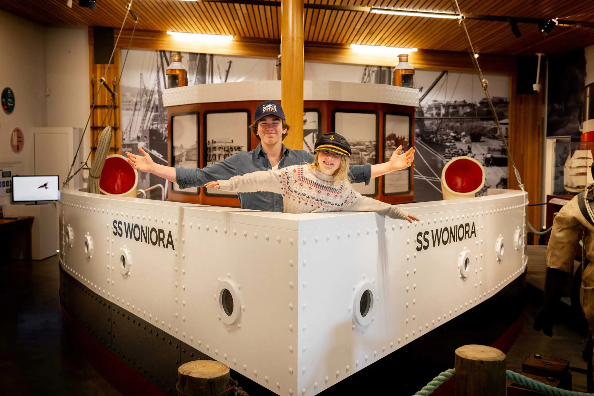 A model of a boat labeled "SS Wonora" inside a museum room. Two people stand at the front of the boat posing with their arms out wide.