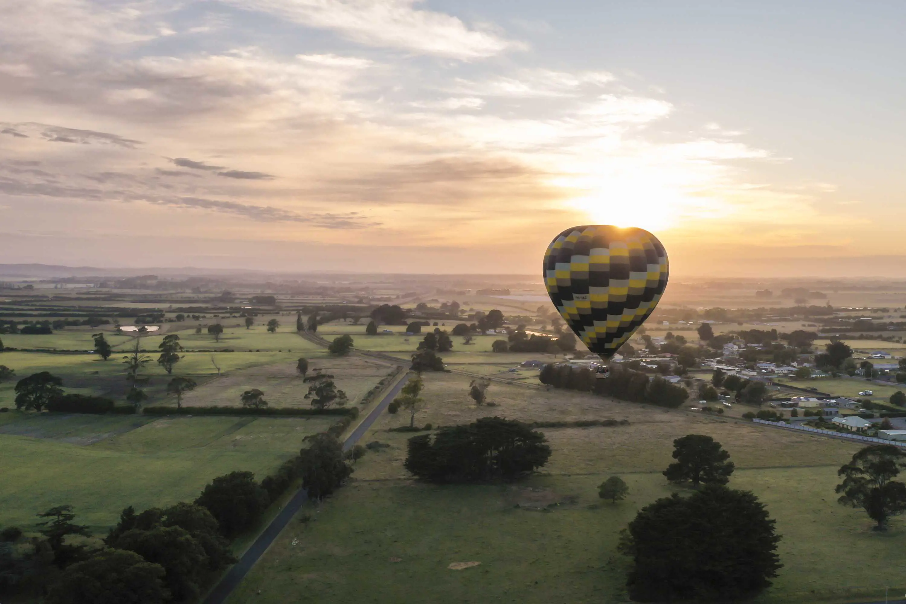 A large air balloon floats above green fields at sunrise.