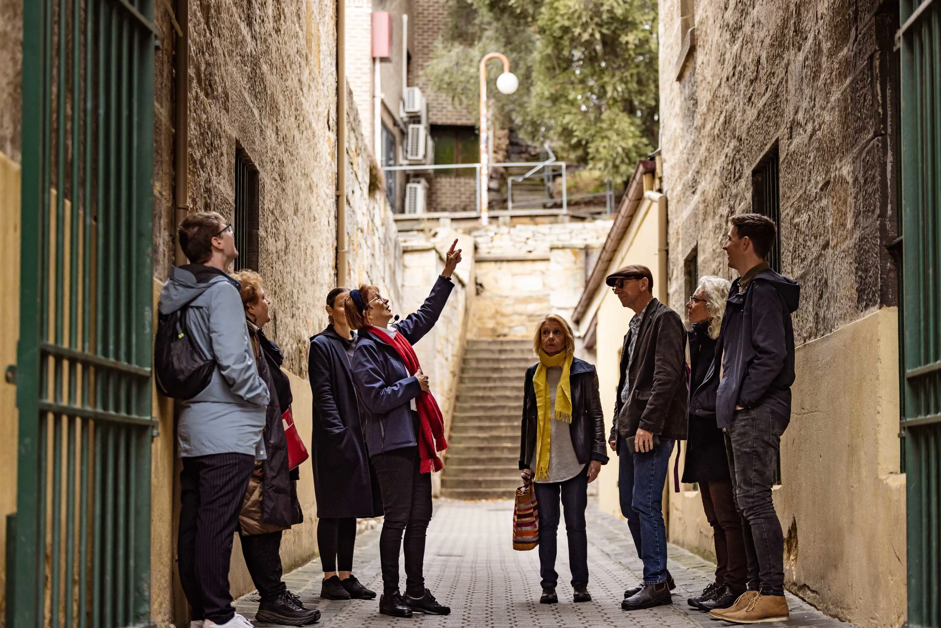 A tour guide speaks to a small group of people in a narrow alleyway that ends in a steep stairwell.